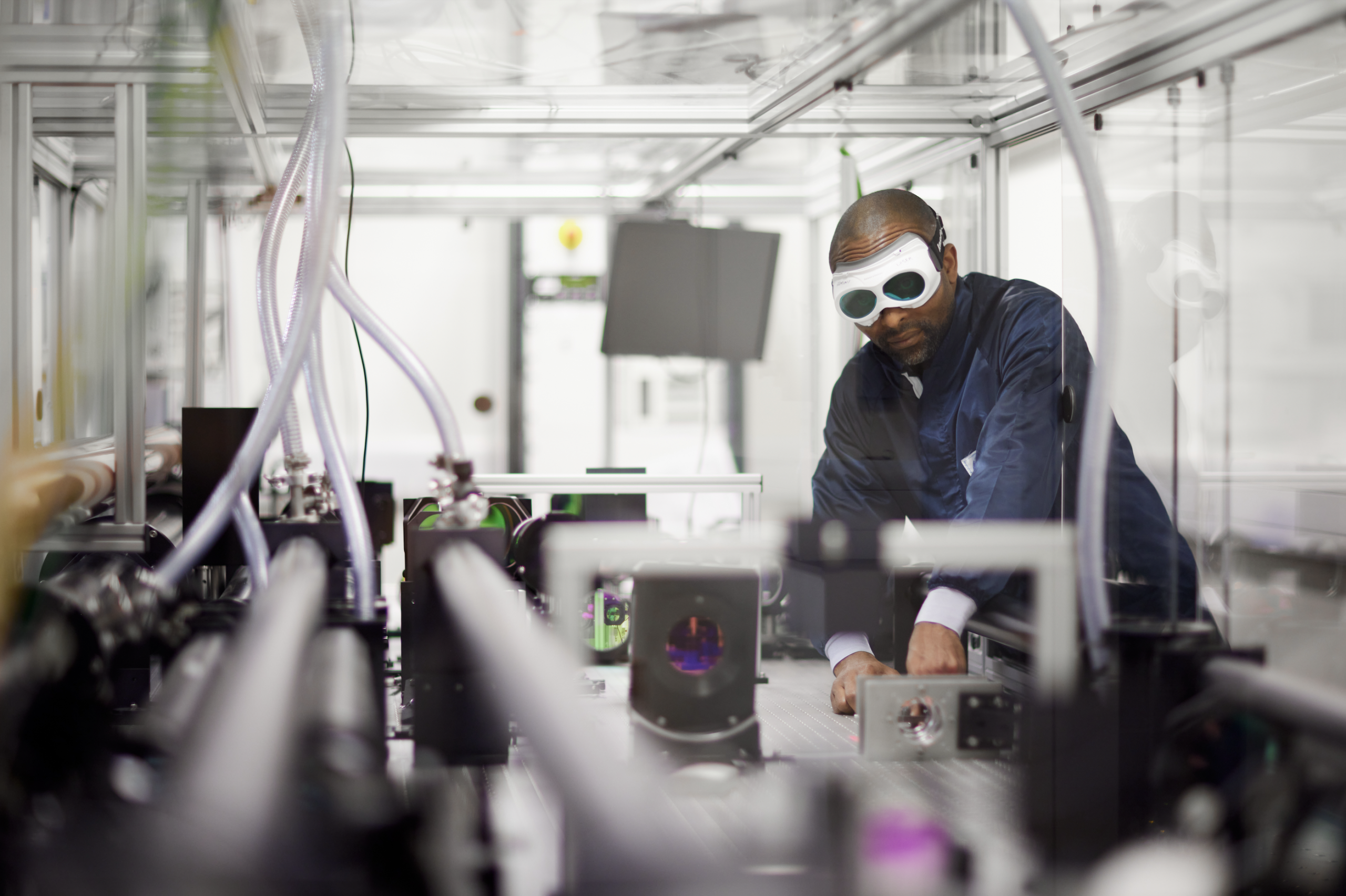 Scientist with laser goggles and a dark blue lab coat works in a lab with lots of chrome.